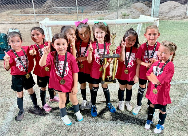 Yuma United players holding up first-place medals around a trophy.